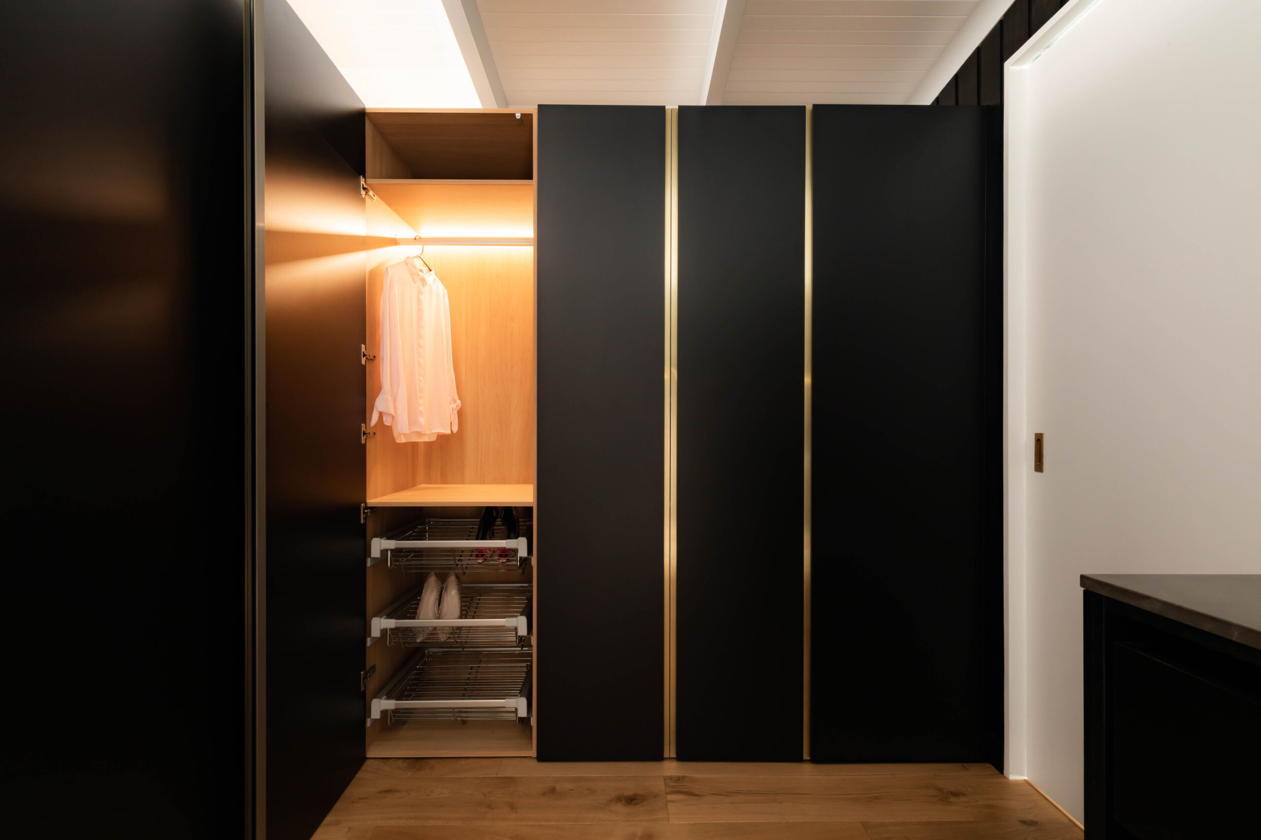 Modern black wardrobe with gold integrated handles and internal LED lighting.