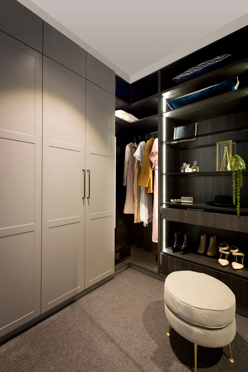 Built-in walk-in wardrobe with shaker style doors, black handles, hanging space, open shelves, drawers and vertical strip LED lighting.